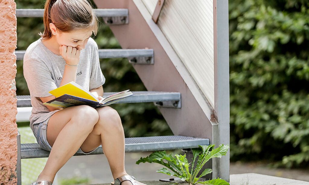 Mädchen sitzt auf einer Treppe und liest ein Buch