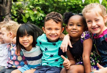 Kinder verschiedener Hautfarben sitzen fröhlich draußen
