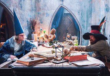 Ein Zauberer und Räuber Hotzenplotz sitzen an einem Schreibtisch und streiten
