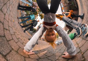Mädchen macht Handstand auf dem Schulhof, mit 360°-Kamera fotografiert und daher rund gebogen