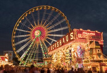 Das beleuchtete Riesenrad und das Glückshaus auf dem Düsseldorfer Kirmesplatz am Abend