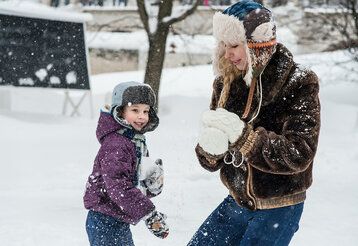 eine junge Frau und ein Kind formen Schneebälle während es schneit