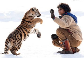 Junge und Tiger spielen im Schnee