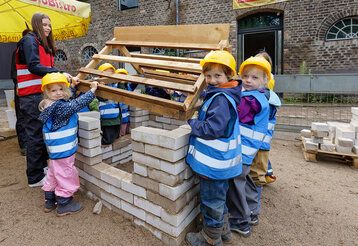 Kinder als kleine Bauarbeiter bauen das Dach von einem kleinen Haus