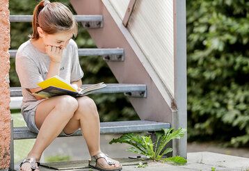 Mädchen sitzt auf einer Treppe und liest ein Buch