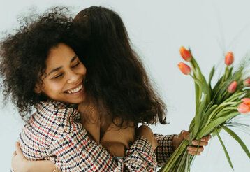 Mutter wird von Tochter umarmt und hält einen Strauß Tulpen in der Hand